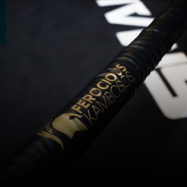 A boxing ring corner pad with "Ferocious Kambosos" written in gold on black leather. The background shows part of the ring mat in dark colors.