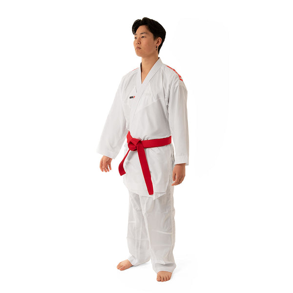 Against a plain white background, a person stands wearing the SMAI WKF Reversible Karate Uniform - 6oz Premium Kumite Gi - Inazuma RX with a red belt. Known for its impeccable fit, they maintain a straight stance with their arms at their sides.