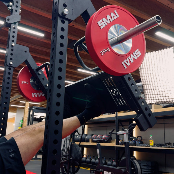 A person uses the SMAI Leg Press Attachment - Vanta Series in a gym filled with diverse equipment, including a power rack and various weights visible in the background.