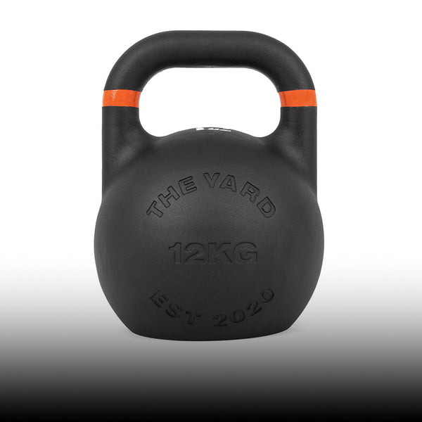 A black 12-kilogram kettlebell with an orange stripe on the handle, featuring embossed text "THE YARD 12KG EST 2020" on the front, against a white-to-black gradient background.