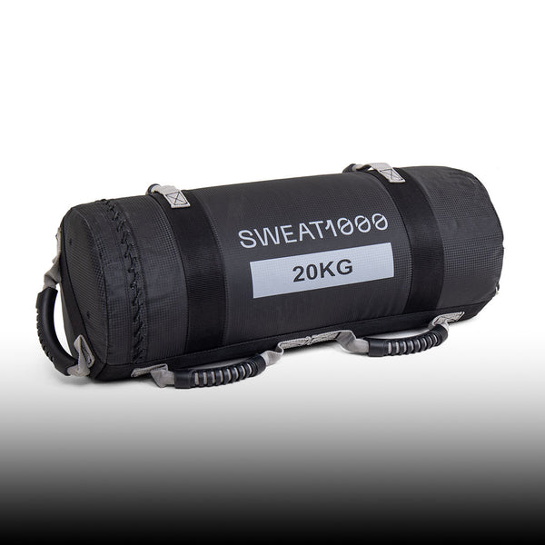 A black cylindrical weighted sandbag labeled "SWEAT1000 20KG" with multiple sturdy handles on the sides, designed for fitness and strength training.