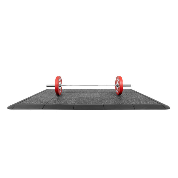 A gym features a barbell with red weight plates on the No Sync To Channel Engine Weight Lifting Platform, Acoustic Rubber White Fleck 50mm. The sectioned, rubber-tiled floor has a beveled edge, designed to stabilize and provide impact protection during weightlifting.
