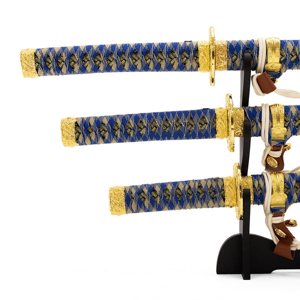 The SMAI Samurai 3pc Sword & Stand - Blue features three decorative Japanese swords with blue and gold handles on a black stand, each displaying intricate patterns—a striking katana set for any collection.