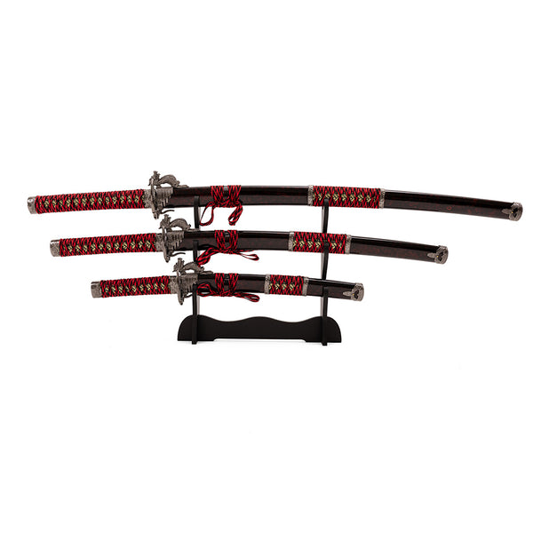 The SMAI Daisho 3pc Set with Stand - Molten Dragon showcases three traditional swords with matching red and gold ornate sheaths, displayed horizontally on a black stand against a white background.