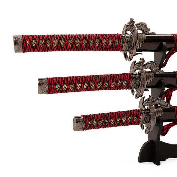 The SMAI Daisho - 3pc Set with Stand – Molten Dragon features three Japanese swords with ornate red and black handles and decorative guards, displayed horizontally on a black stand against a white background.