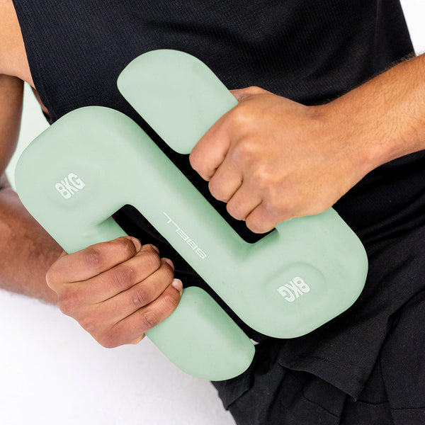 A person wearing a black sleeveless top is holding a pastel green 8 kg weight, designed in the shape of a "U," against their chest, making it ideal for SBELL workouts in a home gym with the SBELL Intermediate pack by No Sync To Channel Engine.