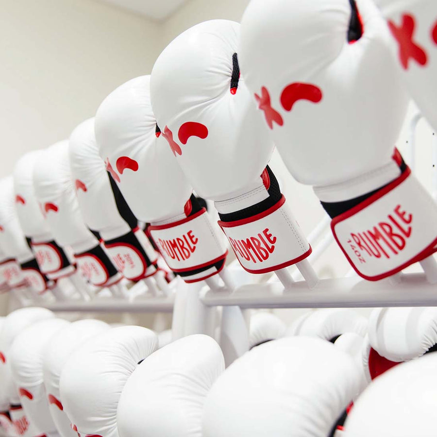 Rows of white boxing gloves with red accents, labeled "RUMBLE," hang neatly on a rack in a bright, clean room.