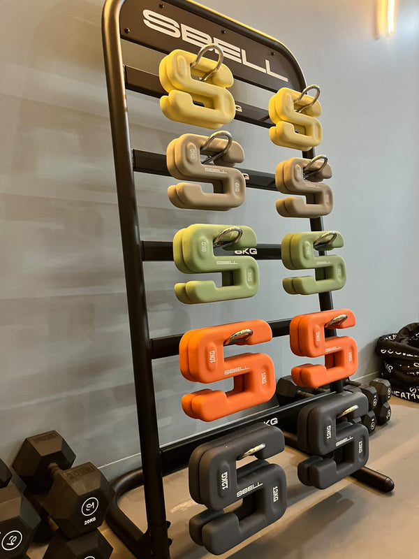 The SBELL Commercial Gym Package from No Sync To Channel Engine showcases a sleek stand that holds a vibrant collection of kettlebell weights in yellow, green, orange, and gray. Ideal for commercial gyms targeting fitness enthusiasts, the setup also includes neatly arranged dumbbells next to the rack.