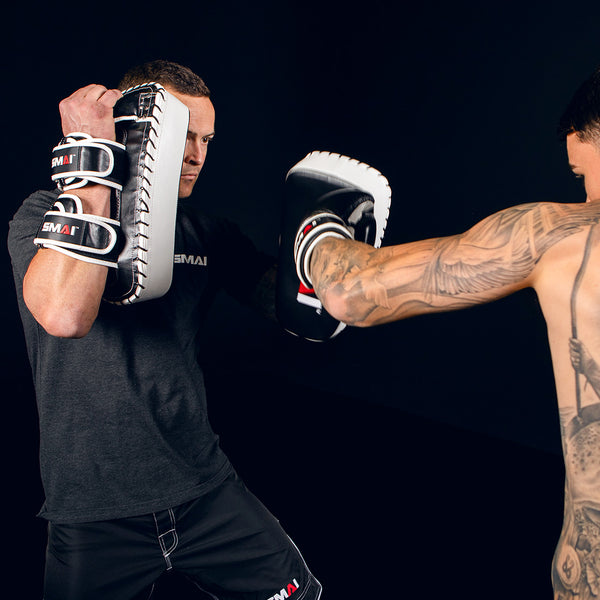 Man Holding Essentials Muay Thai Pads while George Kambosos Jr Punches