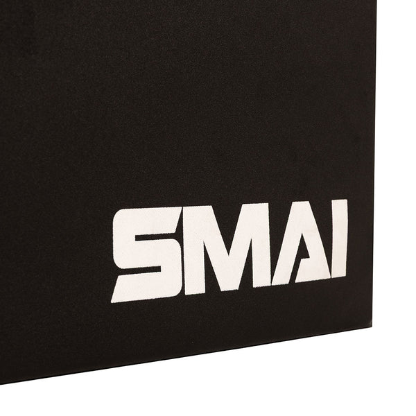 A close-up of a black surface featuring the white “SMAI” logo in the lower right corner showcases the durable build of the SMAI Plyometric Box - Foam Covered - Black Series—an essential piece of equipment for box jumps and other explosive exercises.
