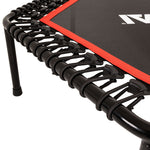 Close-up of the SMAI Rebounder Mini Trampoline 50″ showcases its sturdy metal frame with bungee cords securely attaching the black jumping mat—a durable fitness trampoline featuring a distinctive red border.