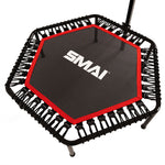 The SMAI Rebounder Mini Trampoline 50″ features a hexagonal design with a black frame, red edging, and a white “SMAI” logo on the jumping surface. Elastic bungee cords securely attach the mat to the frame, providing enhanced bounce and durability for fitness use. A support handlebar is partially visible.