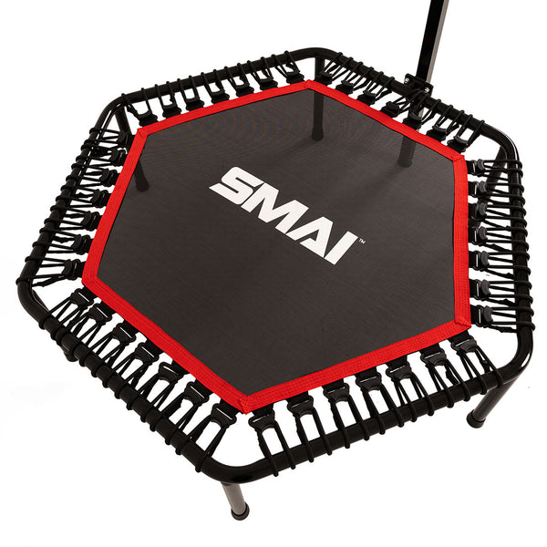 The SMAI Rebounder Mini Trampoline 50″ features a hexagonal design with a black frame, red edging, and a white “SMAI” logo on the jumping surface. Elastic bungee cords securely attach the mat to the frame, providing enhanced bounce and durability for fitness use. A support handlebar is partially visible.