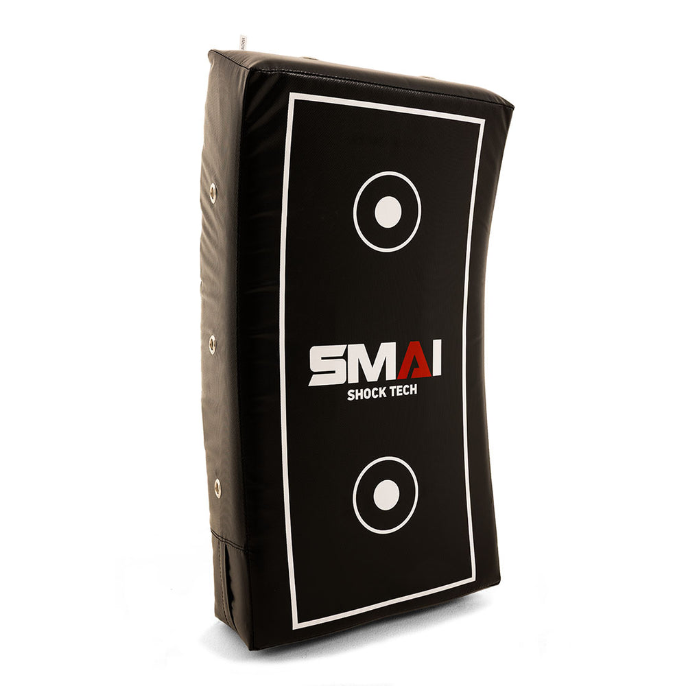 The SMAI Kick Shield - Shoc Tec Curved is a black, lightweight rectangular pad with white target circles and "SMAI SHOCK TECH" text. It features side handles, a slightly curved shape, and impact-absorbing foam for effective training.