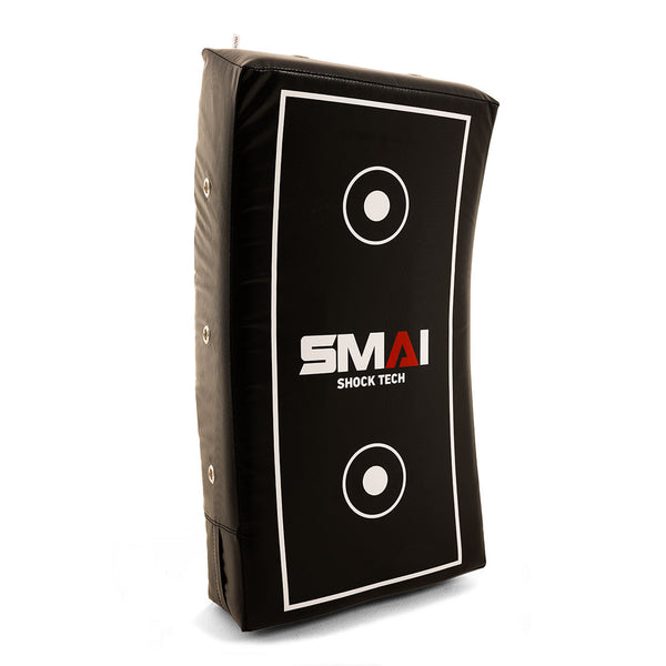 The SMAI Kick Shield - Shoc Tec Curved is a black, lightweight rectangular pad with white target circles and "SMAI SHOCK TECH" text. It features side handles, a slightly curved shape, and impact-absorbing foam for effective training.