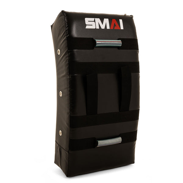 The SMAI Kick Shield - Shoc Tec Curved is a black, rectangular training pad with three horizontal handles, the "SMAI" logo in white and red, a slightly curved shape, visible side stitching, and dense impact-absorbing foam for kicks and strikes.