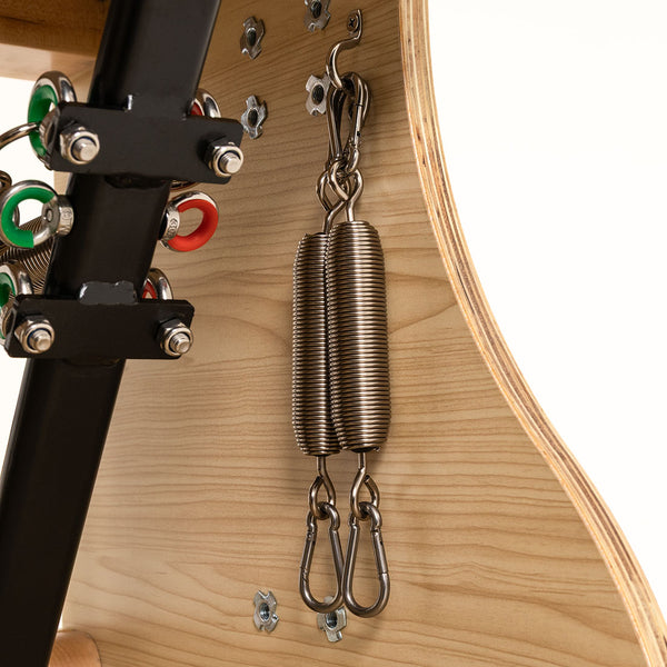 Close-up of two metal tension springs attached to the wooden frame and black metal support of the SMAI Pilates Chair, with visible screws and colored wires—designed for strength training and core conditioning.