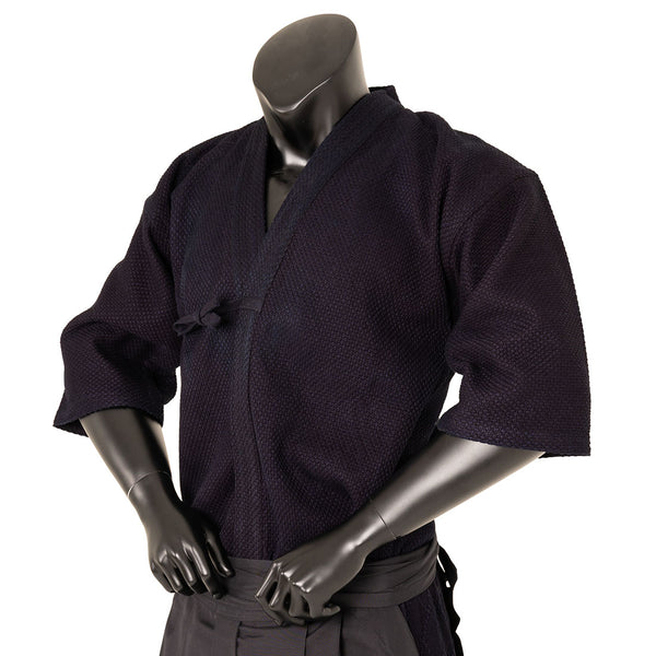 A black mannequin displays the SMAI Deluxe Kendo Jacket—an indigo double layer keikogi crafted from 100% cotton—featuring wide sleeves and a waist tie, with its arms bent and hands resting at the lower front.