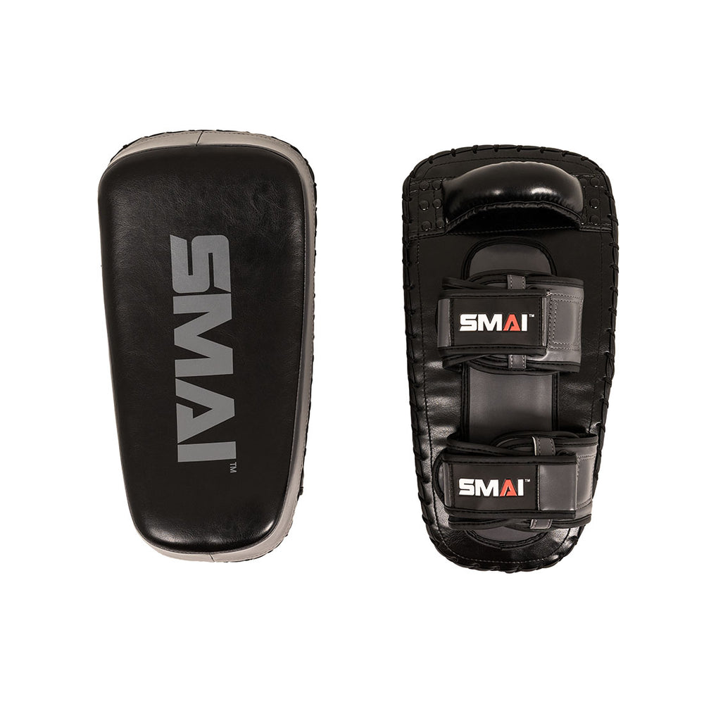 Two grey rectangular Essentials Muay Thai Pads (Pair) from SMAI are made from durable synthetic leather. One pad displays the front with the “SMAI” logo, while the other shows the back, featuring two adjustable straps and a grip handle—ideal for intense kickboxing training or use as Muay Thai pads.