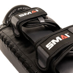 Close-up of an Essentials Muay Thai Pad (Pair) – Economy Grey by SMAI, featuring two straps labeled “SMAI” in white and red on a grey background. Crafted from durable synthetic leather, these pads are ideal for kickboxing training and showcase detailed stitching along the edges.