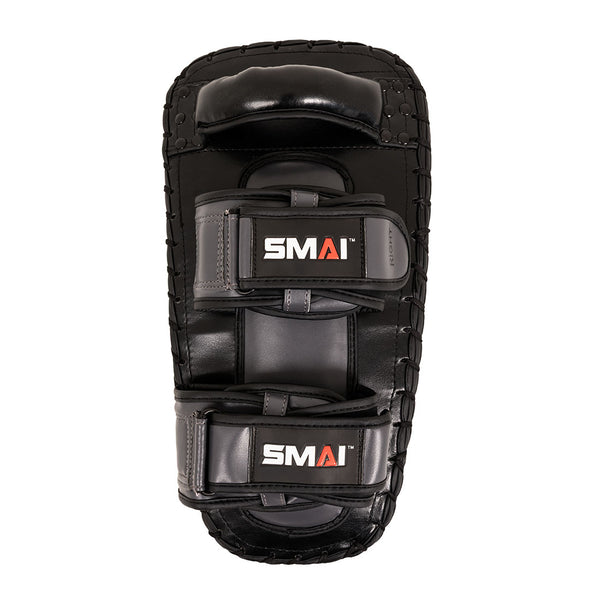 Essentials Muay Thai Pads (Pair) Economy Grey by SMAI—crafted from durable synthetic leather in a sleek black and grey design, these kick pads feature two padded handles and secure arm straps. The “SMAI” logo in white and orange is displayed on both straps. Ideal for kickboxing training, they’re perfect for striking practice and Muay Thai pad drills.