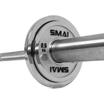 A close-up of a silver Olympic barbell with a 0.5 kg Calibrated Steel Change Plate by SMAI, engraved with the brand name, mounted on the end. The focus is on the plate and collar, showcasing the precision of these powerlifting calibrated plates as the bar extends out of frame.
