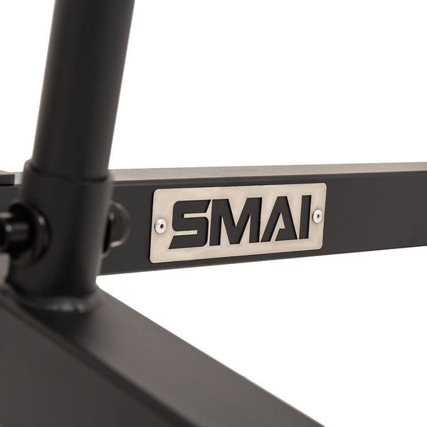 A close-up of a metal frame with a rectangular plate displaying the “SMAI” logo attached with screws, highlighting the sturdy construction of the SMAI Barbell Jack - Double—an essential deadlift jack for effortless weight changes.
