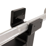 Close-up of a textured metal bar resting in two black, wall-mounted brackets, secured with screws. The bar features a knurled grip pattern for handling—ideal for use with the SMAI Barbell Jack - Double when loading and unloading plates.