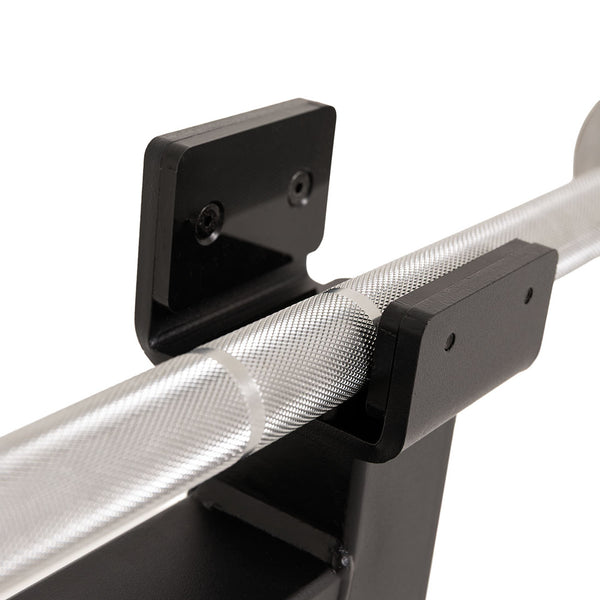 Close-up of a textured metal bar resting in two black, wall-mounted brackets, secured with screws. The bar features a knurled grip pattern for handling—ideal for use with the SMAI Barbell Jack - Double when loading and unloading plates.