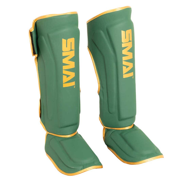 A pair of SMAI Gold Series Muay Thai Shin Guards in green with gold trim and "SMAI" printed in gold on each guard. Designed to cover both the shin and the top of the foot, these shin guards provide reliable padding for enhanced comfort and protection during training sessions.
