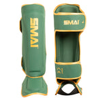 Two SMAI Gold Series Muay Thai Shin Guards in green with gold trim and yellow SMAI branding are shown—one from the front and one from the back—highlighting both shin and foot protection. These guards feature durable EVA padding for enhanced comfort and safety, as well as adjustable straps for a secure fit.