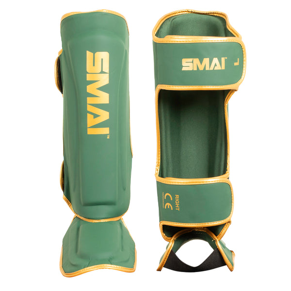 Two SMAI Gold Series Muay Thai Shin Guards in green with gold trim and yellow SMAI branding are shown—one from the front and one from the back—highlighting both shin and foot protection. These guards feature durable EVA padding for enhanced comfort and safety, as well as adjustable straps for a secure fit.