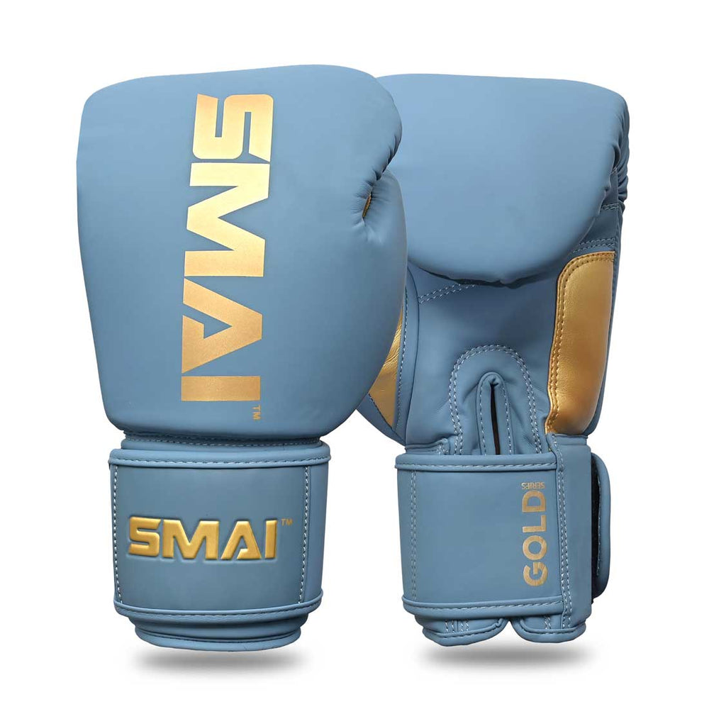 Introducing the SMAI Gold Series Boxing Glove in Light Blue/Gold: featuring gold accents and the "SMAI" logo printed in gold on the top and wrist straps. Designed for superior wrist support, these gloves are displayed upright to showcase both front and side views.