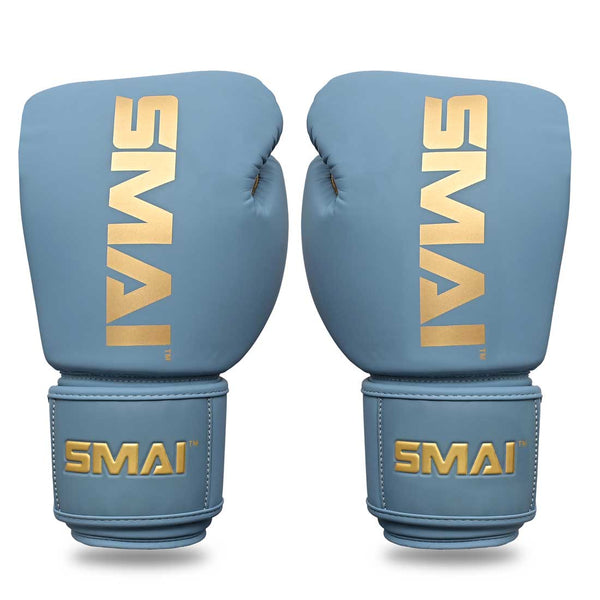 The SMAI Gold Series Boxing Glove in Light Blue/Gold features prominent gold "SMAI" branding on the wrists and backs, displayed upright and facing forward against a white background. These gloves are designed to provide excellent shock protection and superior wrist support for every training session.