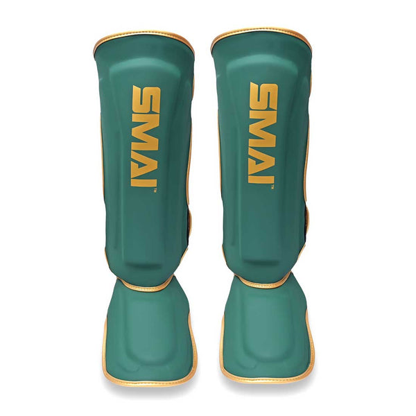 A pair of SMAI Gold Series Muay Thai Shin Guards in green with gold trim, featuring the word "SMAI" printed vertically in gold on the front of each guard. Engineered for optimal safety, these shin guards offer multi-layer EVA protection and high-density foam padding to deliver maximum comfort and impact resistance during training sessions.