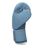 The SMAI Gold Series Boxing Glove in light blue and gold is displayed upright, with the thumb curled in and a Velcro strap around the wrist for enhanced support, isolated on a white background.