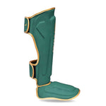 SMAI Gold Series Muay Thai Shin Guards in green and gold, designed with integrated foot protection and multi-layer EVA padding, shown from the side against a white background with an "L" label indicating the left guard.