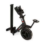 The SMAI AirMag X Rower in a black finish, featuring a large circular flywheel and a digital monitor, shown in a folded, upright storage position.