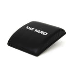 The SMAI The Yard - Ab Mat - Cross Training is a black, slightly curved pad with "THE YARD" in white on top, designed to support your lower back and enhance comfort during ab workouts and CrossFit routines.