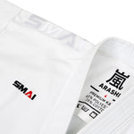 Close-up of a white WKF Karate Uniform by SMAI with the brand name embroidered in black and red on the chest. The inside label, "Arashi," indicates a polyester-cotton blend. Ideal for Karate Federation use, this premium Kata Gi is crafted for performance.