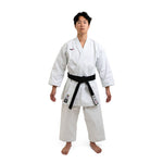 A martial artist in a white SMAI WKF Karate Uniform - Premium Kata Gi - Arashi stands barefoot on a clean backdrop, proudly displaying their black belt and patches on the left side and belt, embodying discipline and focus with a neutral expression.