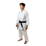 Someone stands in a karate pose, donning an SMAI WKF Karate Uniform - Premium Kata Gi - Arashi with a Japanese style cut and a black belt on a plain white background. Their arms are slightly bent, and their feet are apart, showcasing the WKF Approved attire.