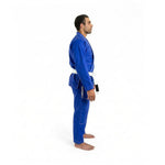 A man stands barefoot in profile, wearing the SMAI Supreme X Brazilian Jiu Jitsu Uniform in blue, made of pearl weave fabric with a white belt, against a plain white background.