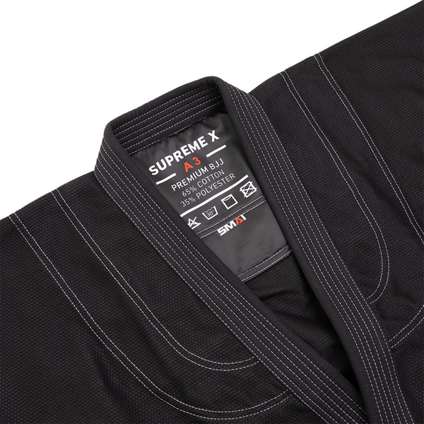 Close-up of the SMAI Supreme X Brazilian Jiu Jitsu Uniform in black, showing white stitching, a pearl weave collar, and an inside label: "SUPREME X PREMIUM BJJ A3, 65% cotton, 35% polyester," care symbols, and the SMAI brand name.