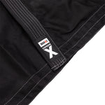 Close-up of the SMAI Supreme X Brazilian Jiu Jitsu Uniform in black, featuring white stitching and durable pearl weave fabric. The "SMAI SUPREME X" tag appears in black, white, and red, highlighting the uniform’s textured details.
