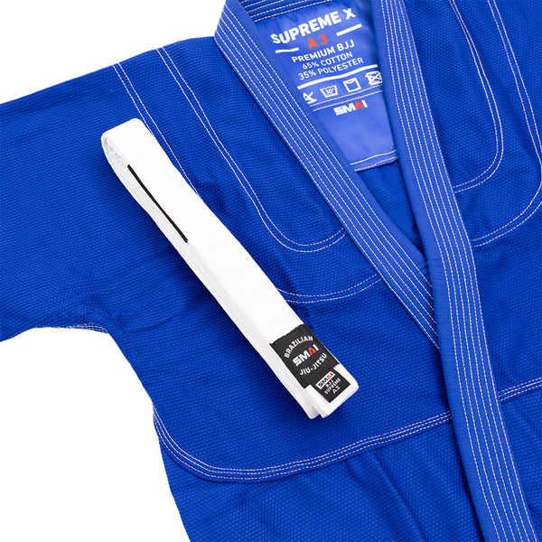 The SMAI Supreme X Brazilian Jiu Jitsu Uniform in blue is laid flat, displaying its pearl weave fabric, Rip Stop pants, and a white belt with a black "Brazilian Jiu Jitsu" label draped over the left shoulder.