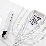 A white SMAI Supreme X Brazilian Jiu Jitsu Uniform, neatly folded with matching belt, features black stitching on pearl weave fabric and a collar label noting 65% cotton/35% polyester.