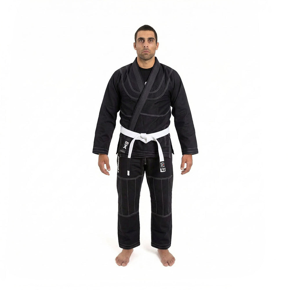 A person stands barefoot with a neutral expression, wearing the SMAI Supreme X Brazilian Jiu Jitsu Uniform - Black, featuring pearl weave fabric and Rip Stop pants, set against a plain white background.