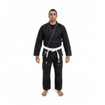 A person stands barefoot with a neutral expression, wearing the SMAI Supreme X Brazilian Jiu Jitsu Uniform - Black, featuring pearl weave fabric and Rip Stop pants, set against a plain white background.