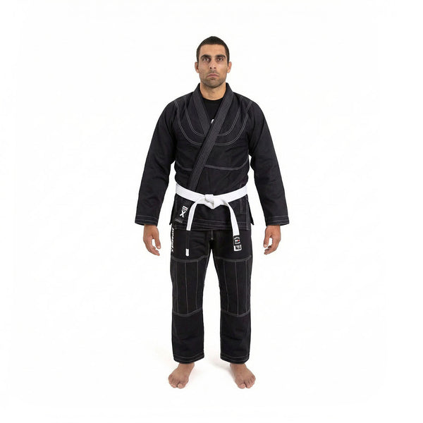 A person stands barefoot with a neutral expression, wearing the SMAI Supreme X Brazilian Jiu Jitsu Uniform - Black, featuring pearl weave fabric and Rip Stop pants, set against a plain white background.